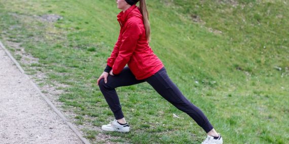 Woman in red jacket stretching in a park, illustrating outdoor fitness and healthy lifestyle.